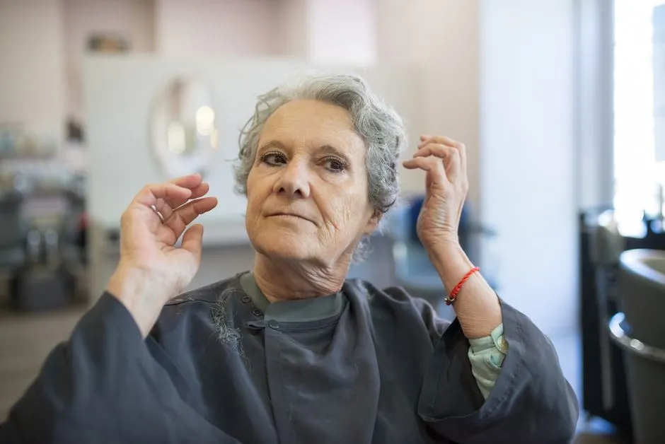 Woman with a short curly gray haircut adjusting her hair in a salon